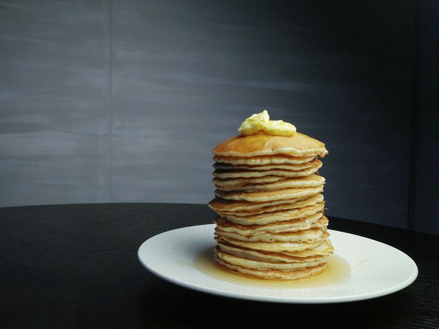 A tall stack of fluffy pancakes topped with butter on a white plate.