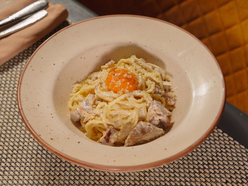 A high-angle view of a classic Italian carbonara pasta topped with a fresh egg yolk.